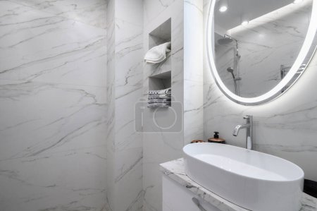 White bathroom interior with marble tiles on the walls and a round mirror