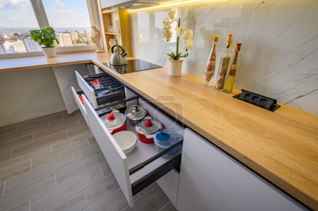A sleek white kitchen with drawers extended to reveal their contents, high angle view