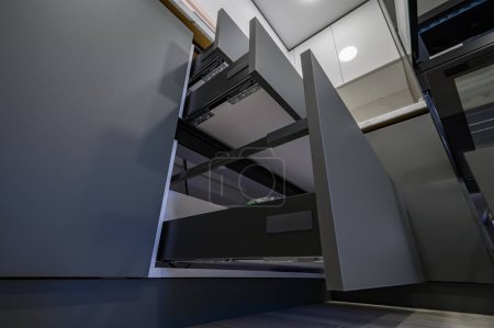 Téléchargez les photos : Closeup details of showcase interior of modern simple dark grey and white kitchen, drawers retracted, low angle view - en image libre de droit