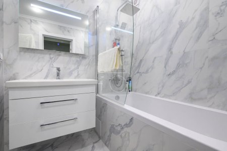 Téléchargez les photos : Salle de bain moderne en marbre blanc avec armoire, miroir de vanité et baignoire - en image libre de droit