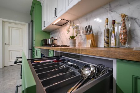 Téléchargez les photos : Closeup to pulled out drawer wih kitchen utensils at new green and white kitchen - en image libre de droit