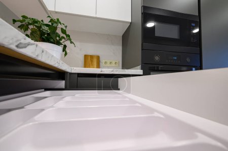 Foto de Closeup to marble worktop of modern dark grey and white kitchen, cooking pan at gas cooker, cabinet drawers retracted - Imagen libre de derechos