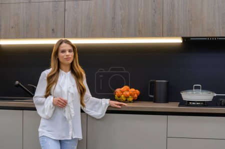 Téléchargez les photos : Young and pretty woman in interior of modern grey large luxurious kitchen - en image libre de droit