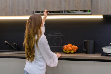 Foto de Young and pretty woman opens cabinet door in interior of modern grey large luxury kitchen - Imagen libre de derechos