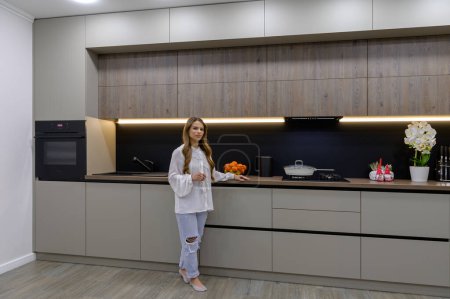 Téléchargez les photos : Young and pretty woman in interior of modern grey large luxurious kitchen - en image libre de droit