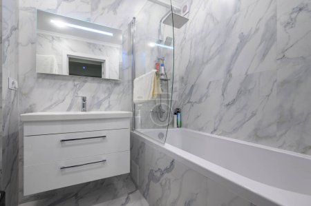 Modern white marble bathroom interior with cabinet, vanity mirror and bathtub