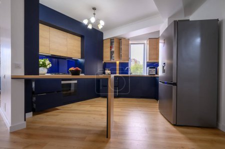 Foto de Luxury large blue and wood colored kitchen in studio apartmentafter good renovation, closeup to counter, some drawers pulled out, unrecognizable person at background - Imagen libre de derechos