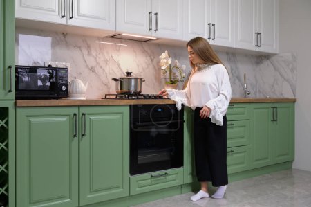 Téléchargez les photos : Young cute woman cooking at new green colored modern well designed kitchen interior after renovation - en image libre de droit