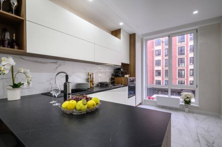 Téléchargez les photos : Intérieur de cuisine moderne de luxe noir et blanc, plan de travail avec fruits et vin au premier plan - en image libre de droit