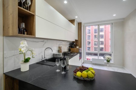 Black and white modern luxury kitchen interior, worktop with fruits and wine in the foreground