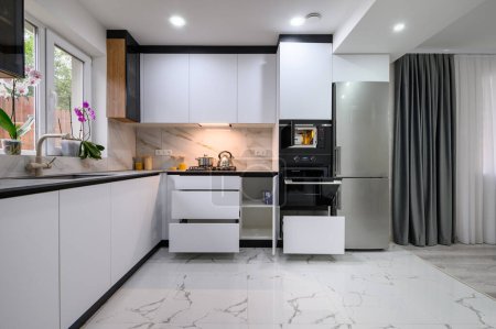Téléchargez les photos : A modern and functional kitchen with a white design, a marble floor, an open oven door, and pull-out shelves for easy access to ingredients and appliances. - en image libre de droit