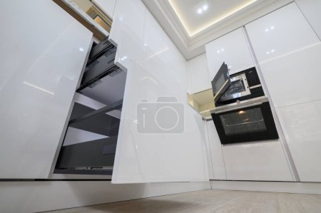 Photo for White modern kitchen with a stove, oven and microwave with open doors, drawers pulled out, high angle view - Royalty Free Image
