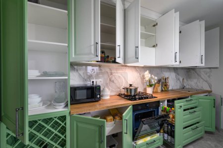 Foto de Doors open and drawers pulled out at new green and white kitchen furniture, showcase interior closeup details - Imagen libre de derechos
