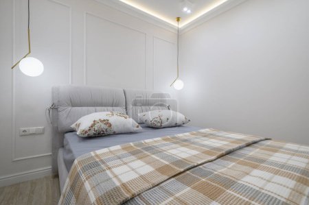 Téléchargez les photos : Gros plan sur lit double avec une couverture à carreaux et des oreillers dans une chambre confortable avec des murs blancs et un luminaire - en image libre de droit