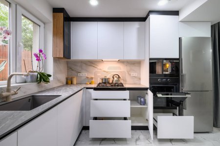 Photo for A spacious and updated kitchen with a white color scheme, a marble floor, an open ovens door, and pull-out shelves for convenient storage and organization - Royalty Free Image
