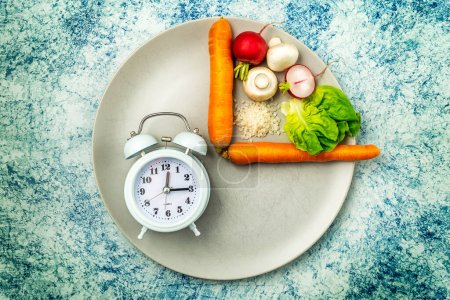 Téléchargez les photos : Intermittent fasting diet concept. One fourth plate with healthy food and three fourths plate is empty. Champignon mushrooms, carrots, lettuce, rice, red radish. Blue rustic background. Top view. - en image libre de droit