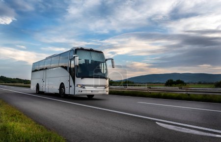 Blanco Moderno autobús turístico cómodo que conduce a través de la carretera en la puesta de sol brillante. Concepto de turismo de viajes y autocares. Viaje y viaje en vehículo
