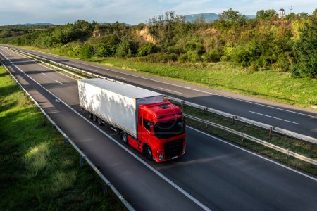 Téléchargez les photos : Grand camion de transport rouge sur une route à travers la campagne - en image libre de droit