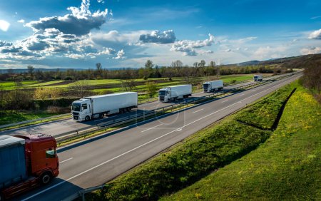 Téléchargez les photos : Scène de transport routier avec convoi de camions de transport blancs en ligne sur une autoroute rurale sous un beau ciel bleu - en image libre de droit