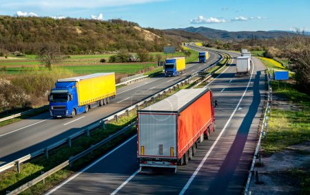 Téléchargez les photos : Convois de transport Camions en lignes se croisant sur une route rurale sous un beau ciel bleu - en image libre de droit