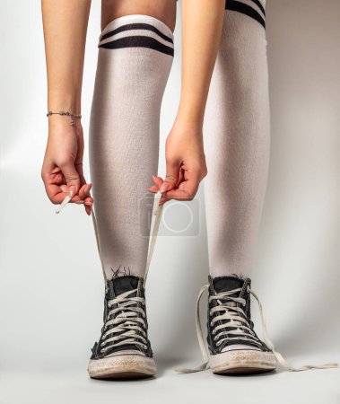 Foto de Las niñas manos atando cordones en viejas zapatillas de deporte azul estilo hipster en las piernas de la chica en sobre los calcetines de rodilla, sobre un fondo blanco - Imagen libre de derechos