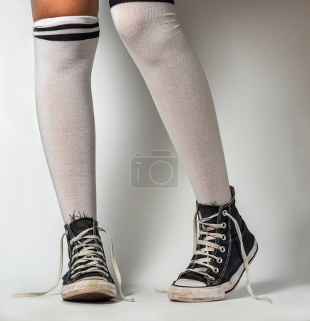 Foto de Viejas zapatillas azules estilo hipster en piernas de niña en sobre los calcetines de rodilla, sobre un fondo blanco - Imagen libre de derechos