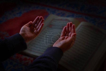Islamisches Foto. Betender muslimischer Mann mit erhobenen Händen. Der Heilige Koran im Hintergrund. Ramadan oder islamisches Konzeptfoto. Selektiver Fokus.