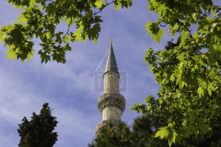 Islamic background photo. A minaret of a mosque with leaves on the tree. Ramadan or islamic concept.