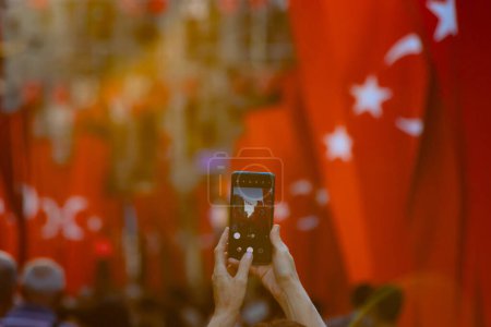 Photo for Woman taking photo of a street full with people and Turkish flags. National holidays of Turkiye concept photo.. Selective focus on foreground. - Royalty Free Image
