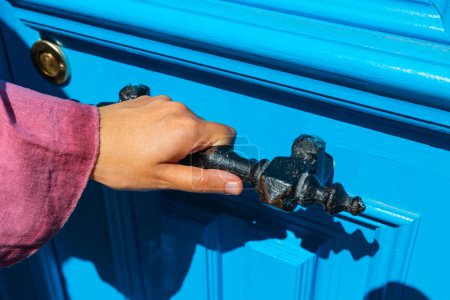 Mujer sosteniendo una manija de puerta oxidada vintage para entrar en la casa.