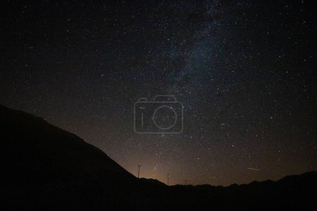 Milky way over the silhouette of the hills and city lights at night. Astrophotography concept photo. Noise included.
