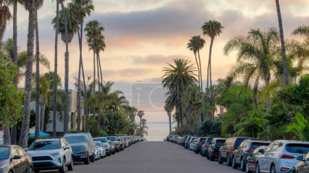 Panorama Nuages gonflés au coucher du soleil Véhicules stationnés sur la route asphaltée près de la baie de La Jolla, Californie. Il y a deux voies de véhicules des deux côtés de la route avec des palmiers contre la vue sur un océan et le ciel.