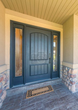 Photo for Vertical Porch of a house with stone tiles flooring and black front door with two side panels. Exterior of a house with stone veneer siding and railings on the left. - Royalty Free Image