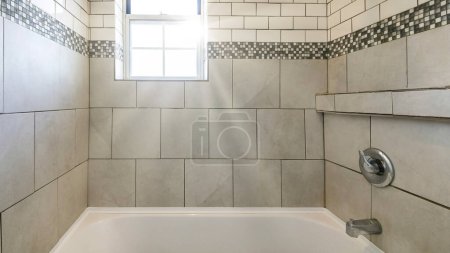Photo for Panorama Sun flare Alcove bathtub shower combo with ceramic and subway tiles wall with mosaic tiles trim in the middle. Bathtub with wall mounted shower head and faucet near the single hung window at the front wall. - Royalty Free Image