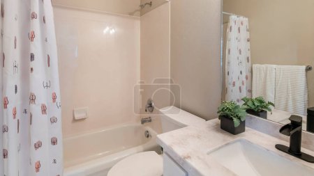 Photo for Panorama Small modern traditional bathroom interior with tub-shower combo kit. There is a vanity sink with potted plant on the marble top near the toilet and bathtub with printed doodles on the shower curtain. - Royalty Free Image