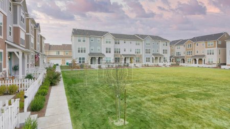 Photo for Panorama Puffy clouds at sunset Large lawn field in the middle of townhouse buildings. Residential complex buildings with different structures and white picket fences at the front. - Royalty Free Image