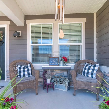 Photo for Square Nice front porch with potted flowers and two woven arm chairs. There is a table with ornaments in between the chairs at the front of the window near the black front door on the left with wreath. - Royalty Free Image