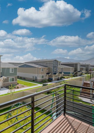 Photo for Vertical White puffy clouds View of the neighborhood houses with lawn and concrete paths from a deck. Deck of a fenced house with wooden flooring and metal railings with a view of the yard with - Royalty Free Image