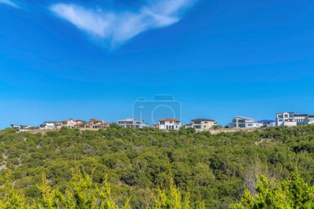 Photo for Beautiful residential houses on a hill at Comanche Canyon Ranch in Austin Texas. Facade of distant homes along the bakns of Lake Austin with lush foliage in the foreground. - Royalty Free Image