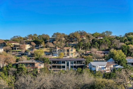 Photo for Austin, Texas- Facade of large houses on a sloped residential area near Lake Austin. Rich neighborhood surrounded by trees and plants and a blue sky background. - Royalty Free Image