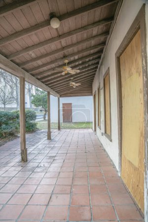 Foto de San Antonio, Texas- Suelos de baldosas rojas de un porche de un edificio abandonado con pilares de madera. Casa abandonada con ventanas y puertas tapiadas. - Imagen libre de derechos