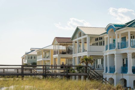 Destin, Florida- Footbridge with stairs on a white sand dunes of a beach at the front of houses. Row of beach houses with terraces.