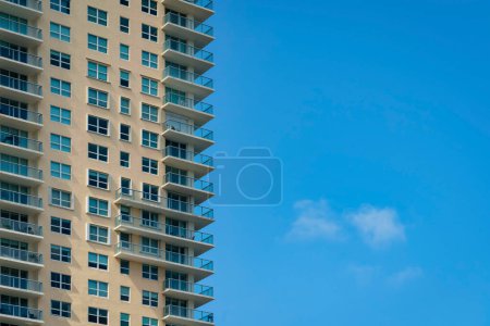 Photo for Facade of a condominium with beige wall exterior and glass railings on the balconies- Miami, Florida. View of a multi-storey modern residential building on the left and clear blue sky on the right. - Royalty Free Image