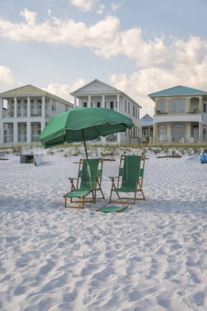Foto de Destin, Florida- Sillones verdes al aire libre bajo el paraguas en una arena de playa blanca. Dos sillones en la parte delantera de las casas de playa con balcones. - Imagen libre de derechos