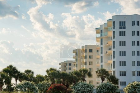 Photo for Trimmed bougainvillea and palm trees at the front of apartments in Destin, Florida. Row of apartments with balconies against the cloudy sky background. - Royalty Free Image