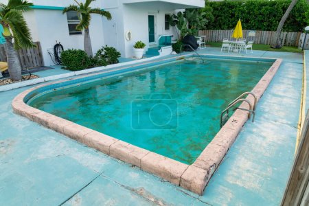 Foto de Sucia piscina privada al aire libre con algas cerca de las plantas y árboles fuera del edificio en Miami, FL. Hay una mesa con sillas con paraguas cerca de la valla al lado de la piscina en la parte posterior. - Imagen libre de derechos