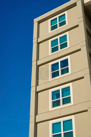 Photo for Building exterior with square paned windows in a low angle view at Destin, Florida. View of a dark beige building against the clear blue sky background. - Royalty Free Image