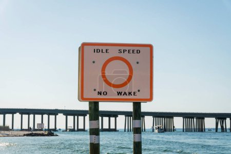 Téléchargez les photos : Idle Speed No Wake Connectez-vous dans une voie navigable sous le pont de Destin, en Floride. Gros plan d'une signalisation dans une zone à basse vitesse sous le pont à l'arrière contre le ciel clair. - en image libre de droit