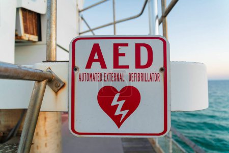 Foto de Destin, Florida- AED Señalización automatizada del desfibrilador externo en un muelle. Primer plano de un cartel en una barandilla de acero y una vista del océano al fondo. - Imagen libre de derechos