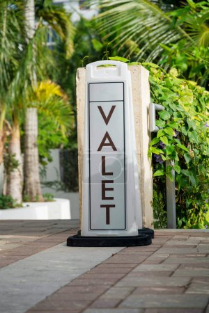 Photo for Floor-mounted Valet signage on a bricks pavement- Miami, Florida. Valet sign near the railings with crawling plants on the right and views of trees on the left. - Royalty Free Image